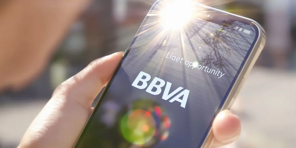 Persona sonriente sosteniendo un teléfono con un logotipo de BBVA.